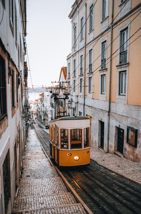 A yellow tram travels down a narrow, cobblestone street lined with buildings in Lisbon.