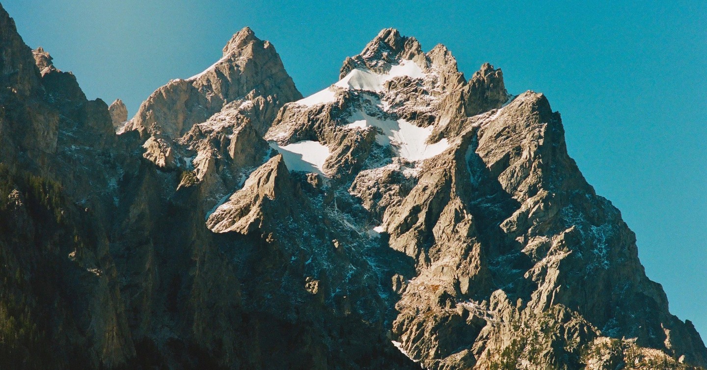 A rugged mountain range with patches of snow is visible under a clear blue sky.