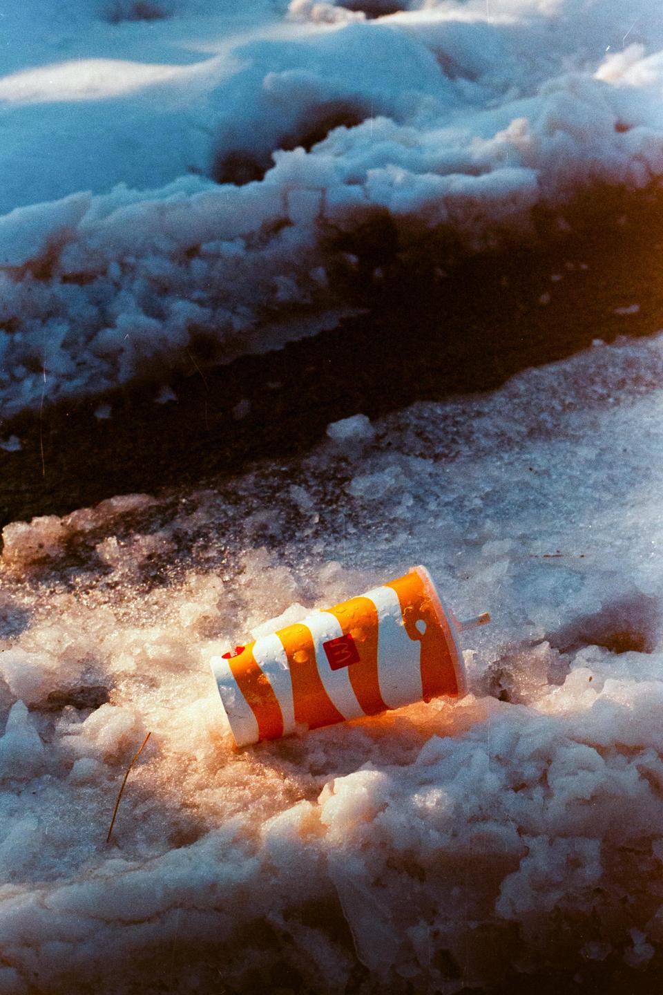 A discarded fast food cup lies in dirty snow.