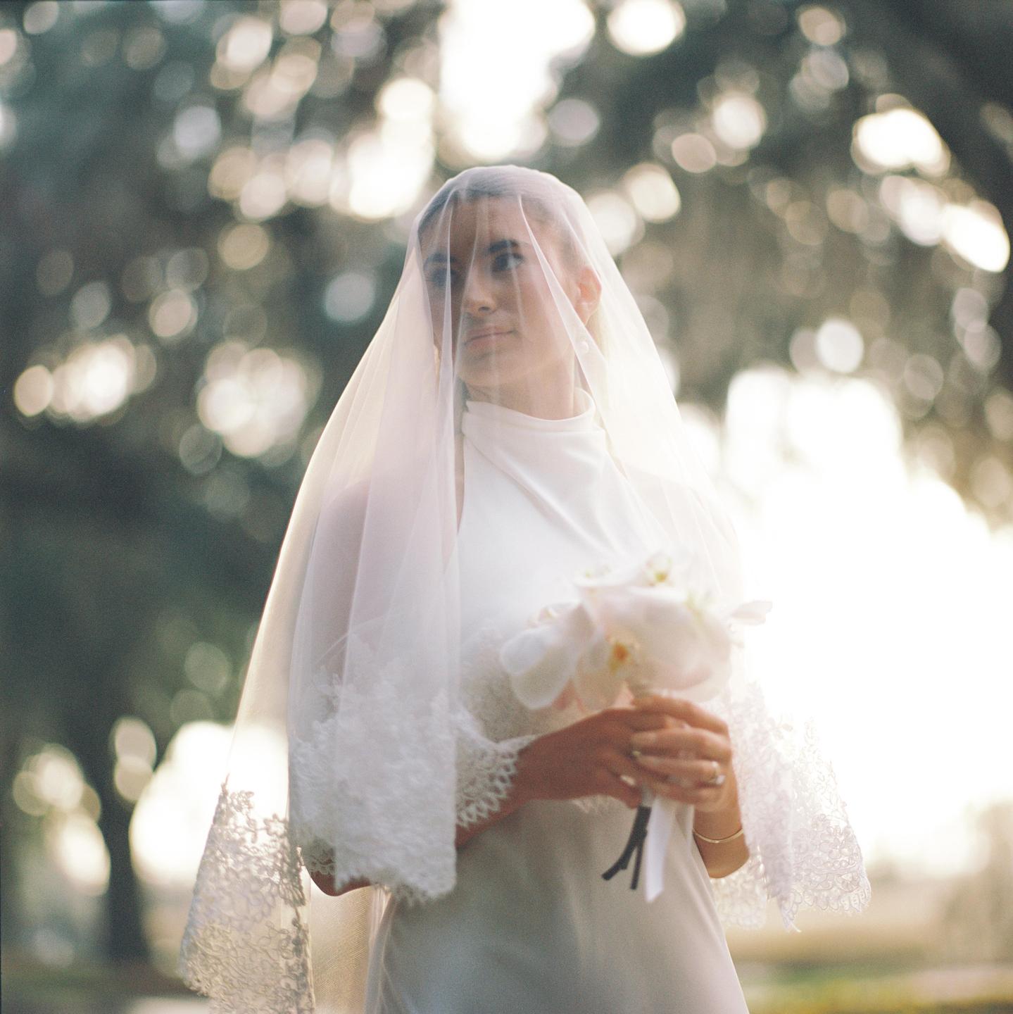 A woman in a white dress and veil holds a bouquet of white flowers.