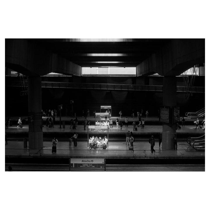 People wait on a subway platform in a black and white image.