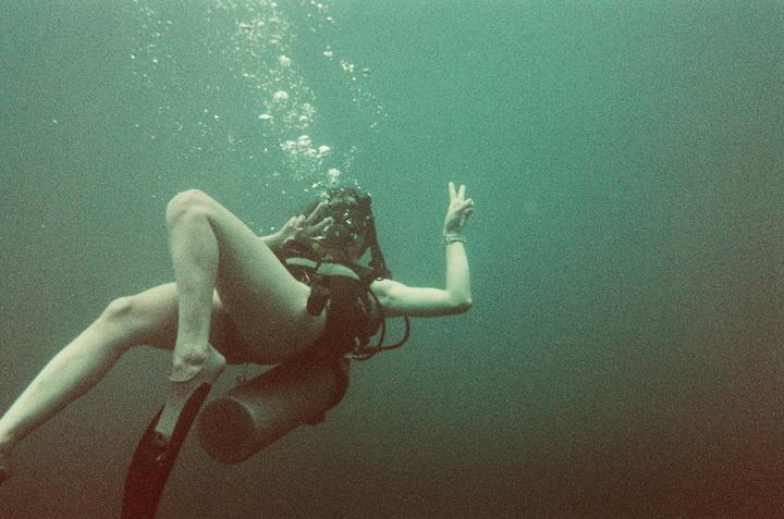A woman scuba diver floats underwater, making a peace sign with both hands.
