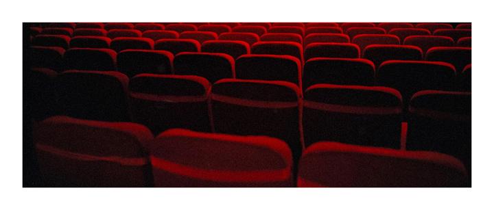 Rows of empty red seats are visible in a dark theater.