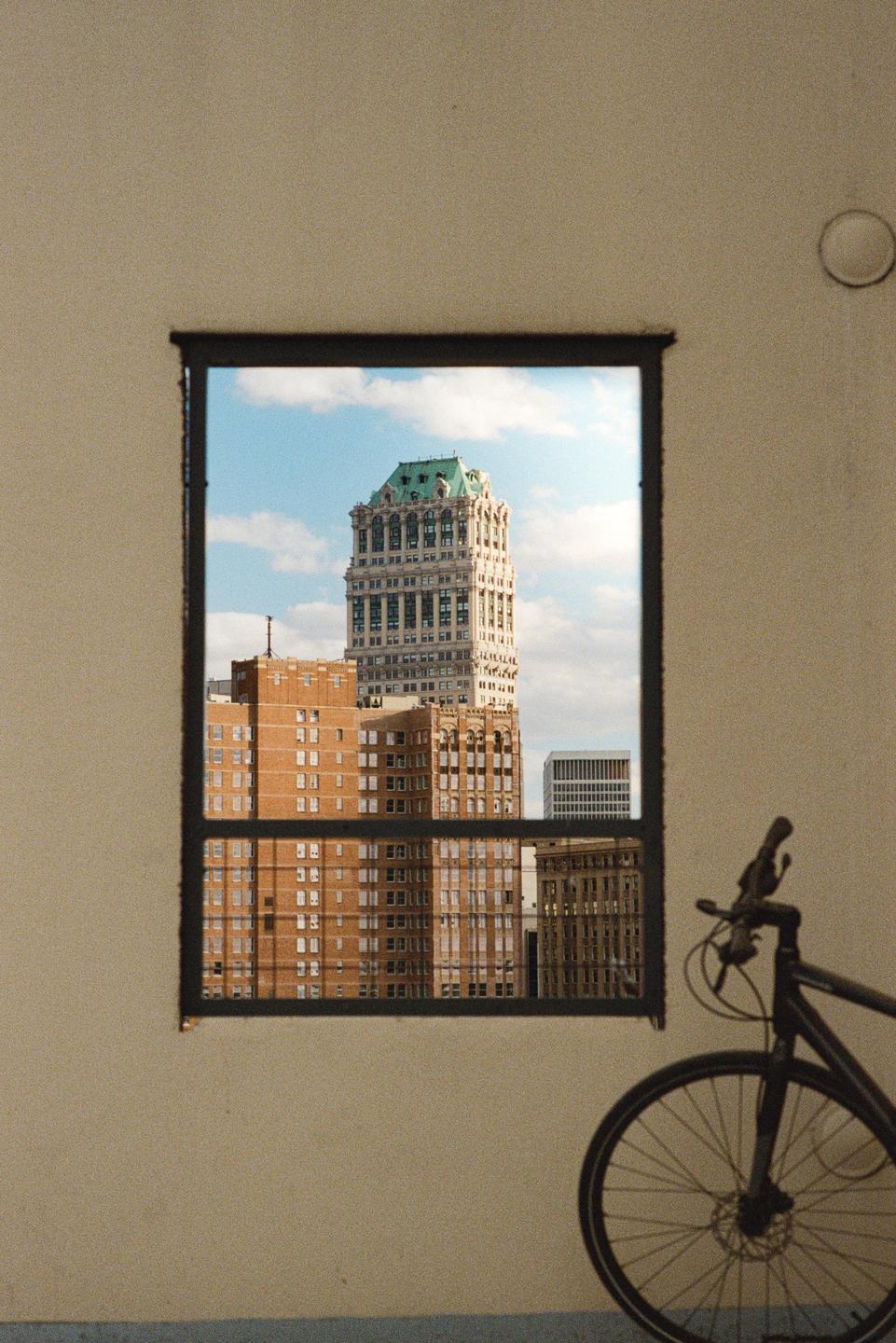 A tall building with a green roof is visible through a window, with a bicycle parked to the right.