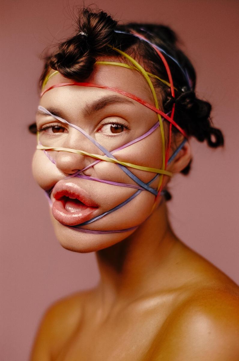 A woman's face is distorted by colorful rubber bands wrapped around her head.