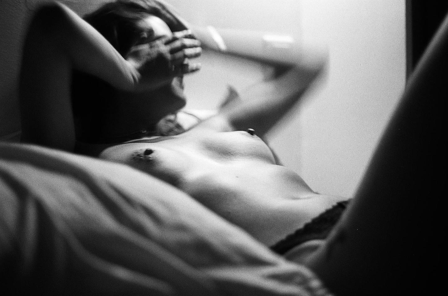A woman lies on her back with her arms raised and hands covering her face.