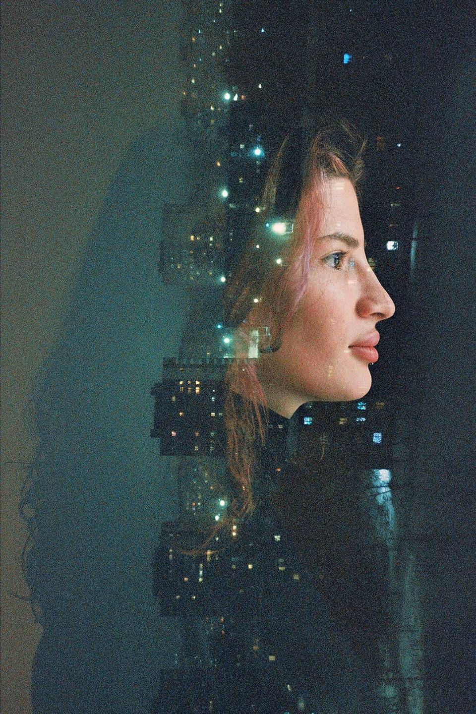A woman's profile is superimposed over a city nightscape with illuminated windows.