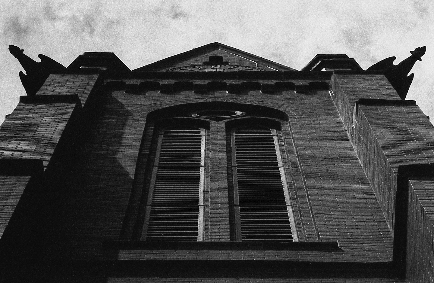A low-angle view shows the brick facade of a building with two tall windows and two gargoyles on the roofline.