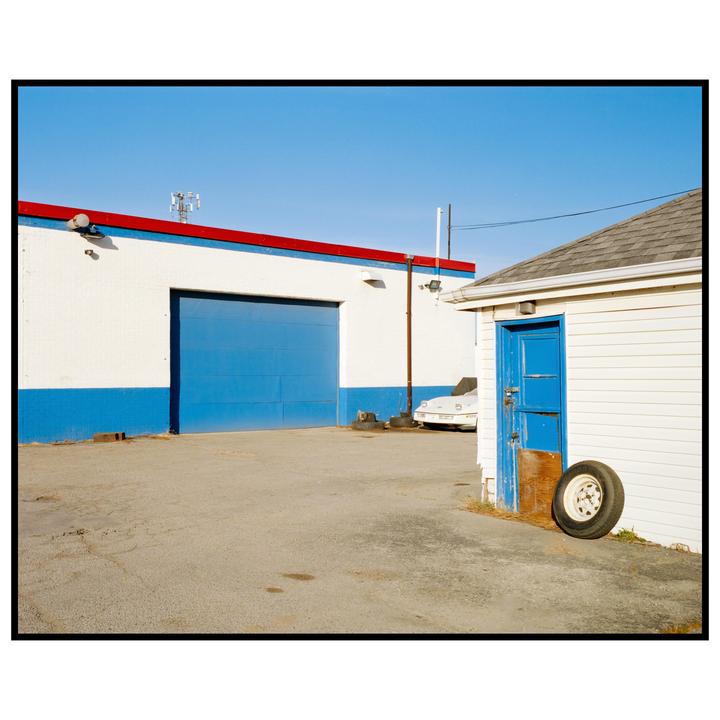 A white building with a blue garage door and a smaller white building with a blue door are visible under a clear blue sky.