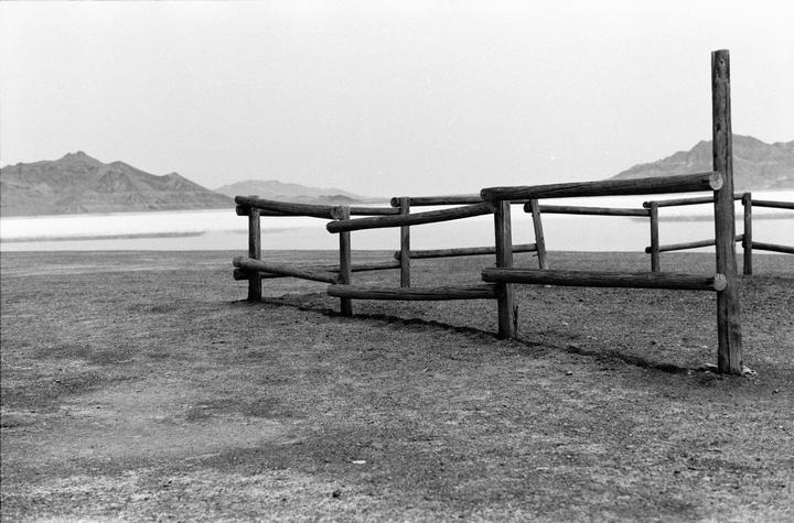 A wooden fence stands in the foreground with a body of water and mountains in the background.
