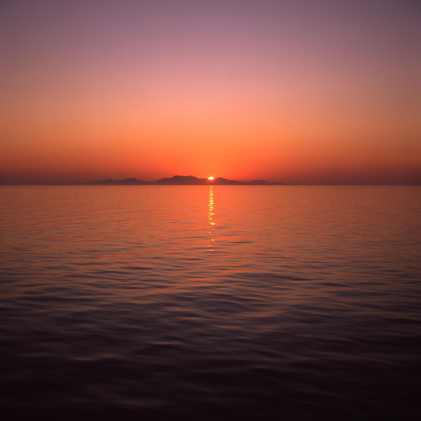 The sun rises over a body of water with mountains in the distance.