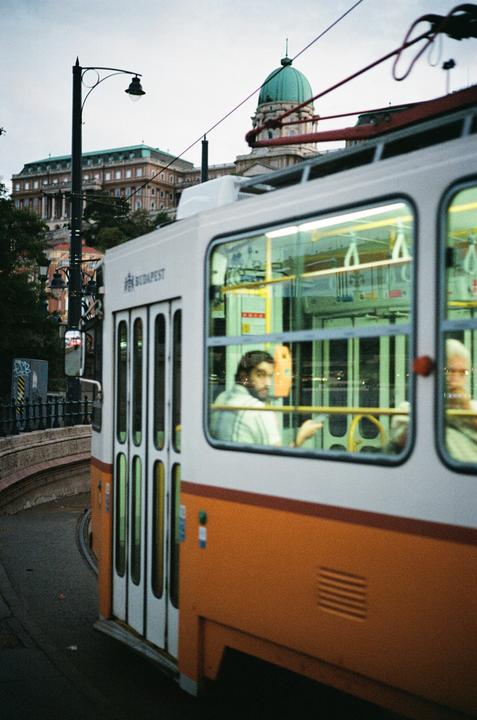 A tram with passengers inside is turning on a street with a large building and dome in the background.