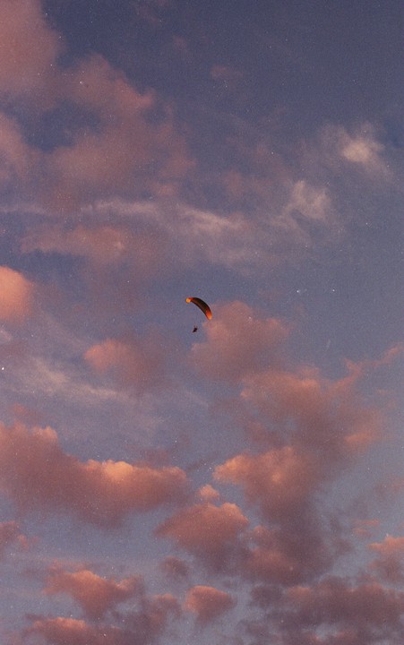 A paraglider soars through a sky filled with pink and purple clouds.