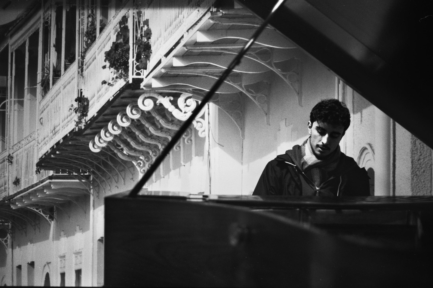 A man sits at a piano with ornate balconies in the background.