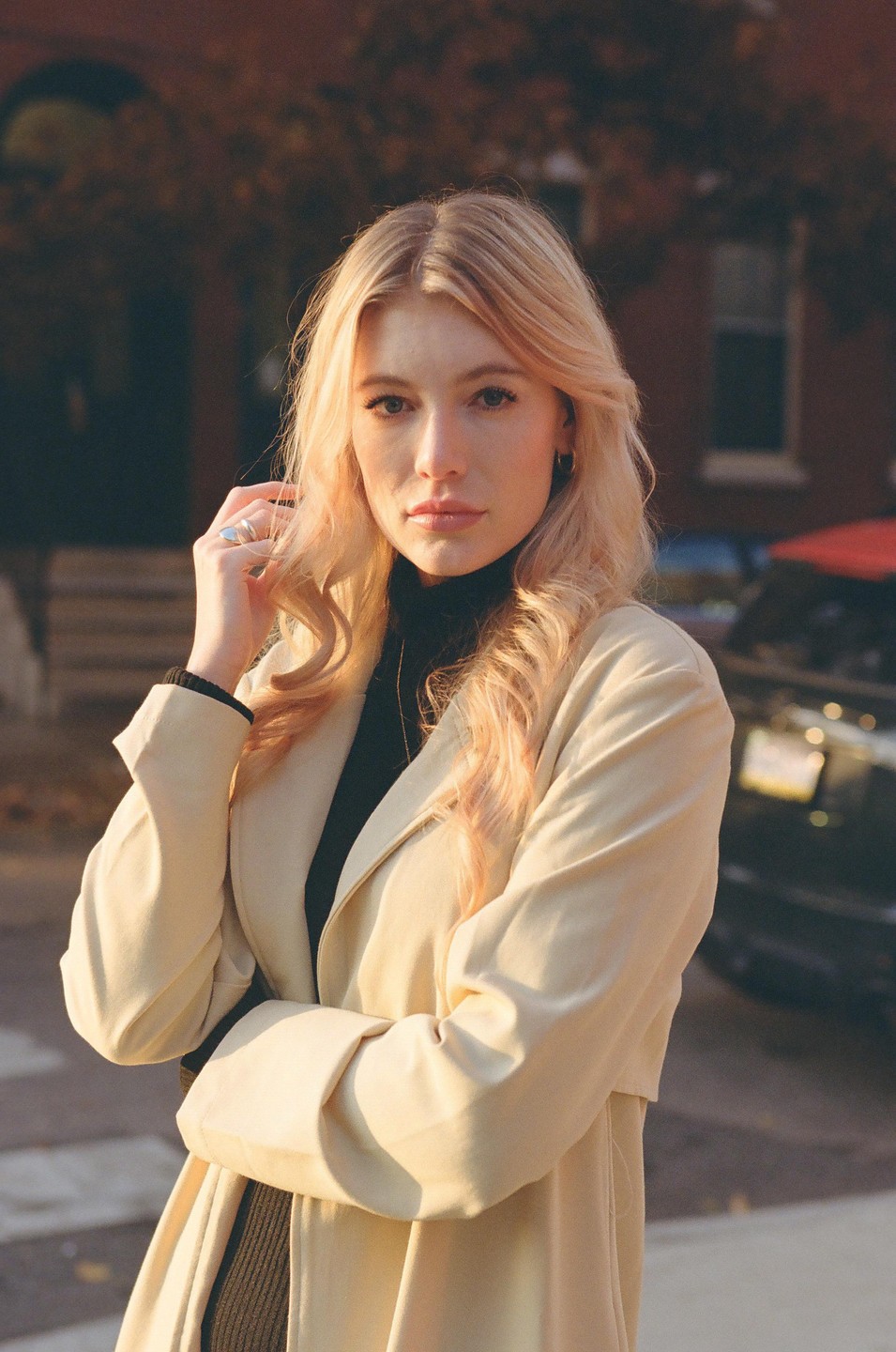 A woman with long blonde hair and a light-colored coat stands on a street.