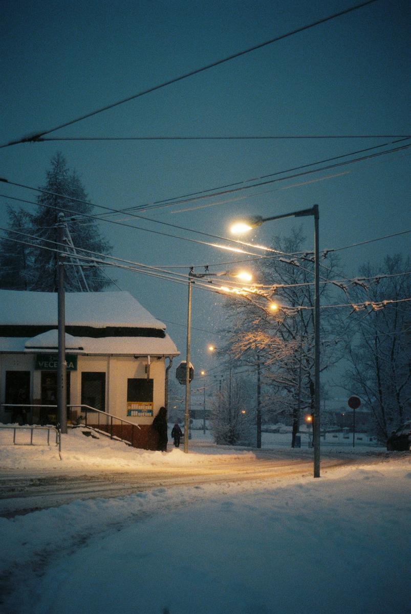 A snow-covered street with a building on the left and streetlights illuminating the scene at night.