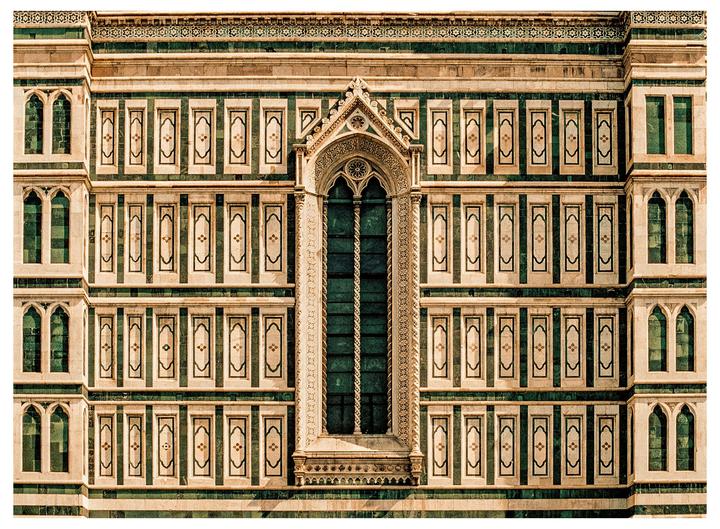 A large ornate window is centered on a building facade with many smaller windows and decorative panels.