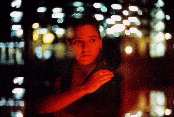 A woman with a ring on her finger is illuminated by red light with bokeh lights in the background.