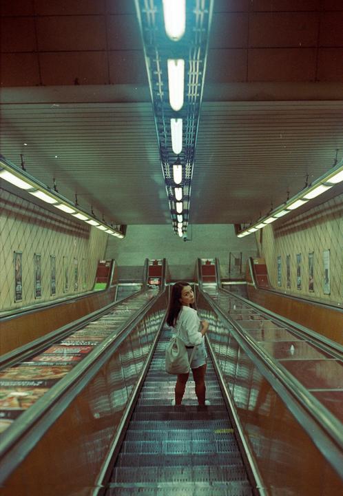 A woman stands on an escalator in a subway station, looking back at the camera.