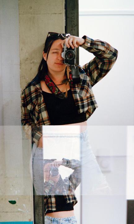 A woman takes a mirror self-portrait, with a double exposure effect showing her reflection overlapping her body.