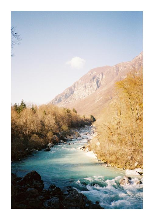A turquoise river flows through a valley with mountains and bare trees under a clear sky.