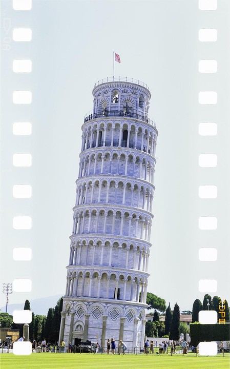 The Leaning Tower of Pisa stands tall with a red flag on top, surrounded by a green lawn and people.