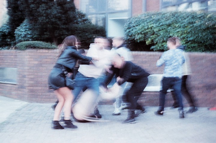 A blurry street photo captures a group of young people in motion, with a woman in a leather jacket and skirt in the foreground.