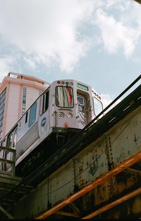 A train is visible on an elevated track with a building and cloudy sky in the background.