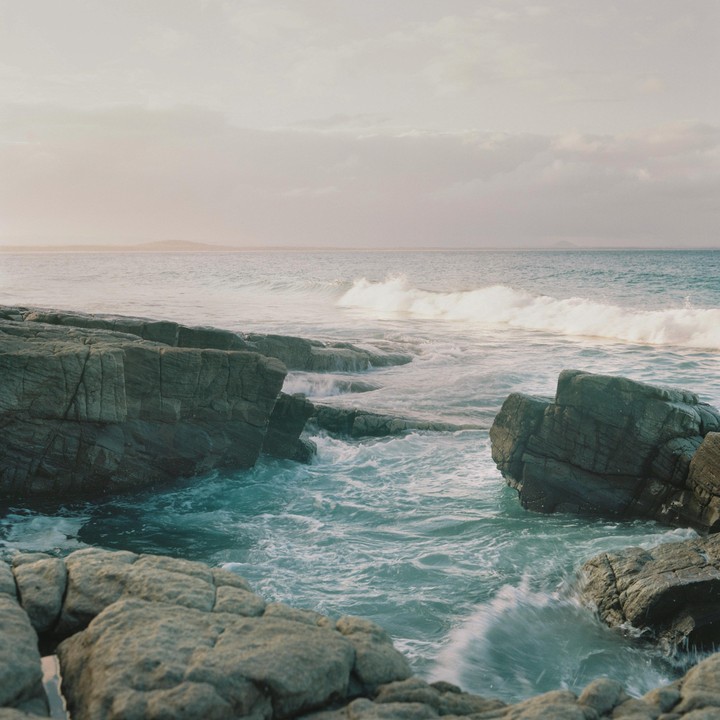Waves crash against a rocky shore under a cloudy sky.