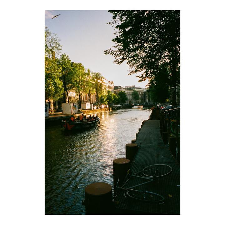 A boat with people travels along a canal lined with buildings and trees at sunset.