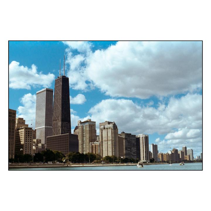 A wide shot of the Chicago skyline with a body of water in the foreground and a cloudy sky above.