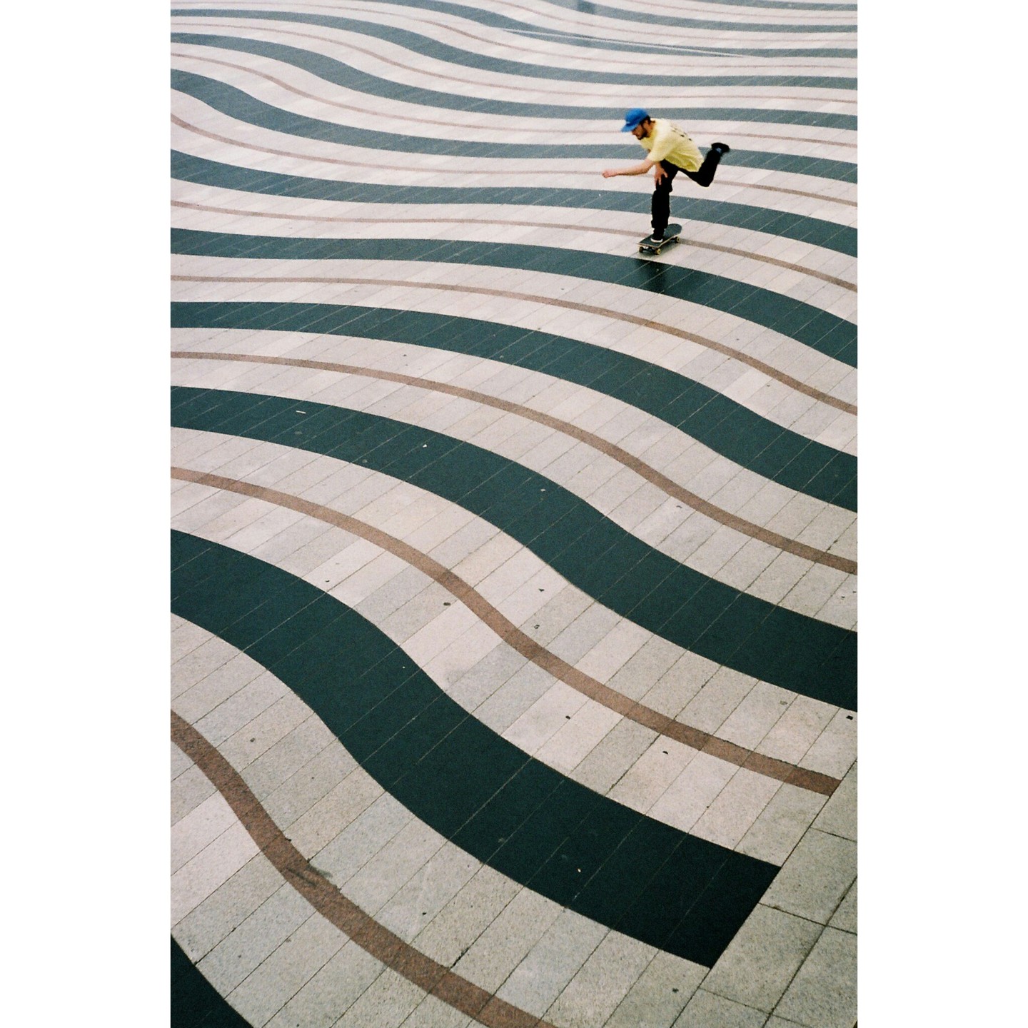 A man on a skateboard pushes across a patterned ground with wavy stripes.