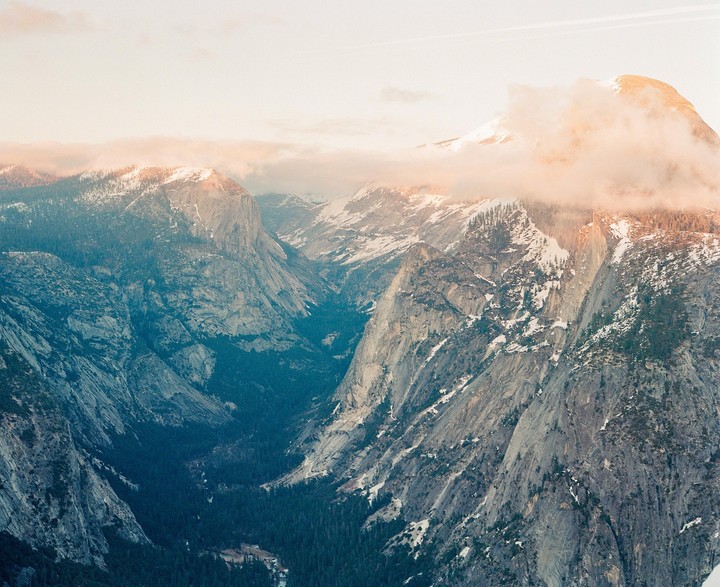 Clouds partially obscure a snow-capped mountain peak and a valley with a river.