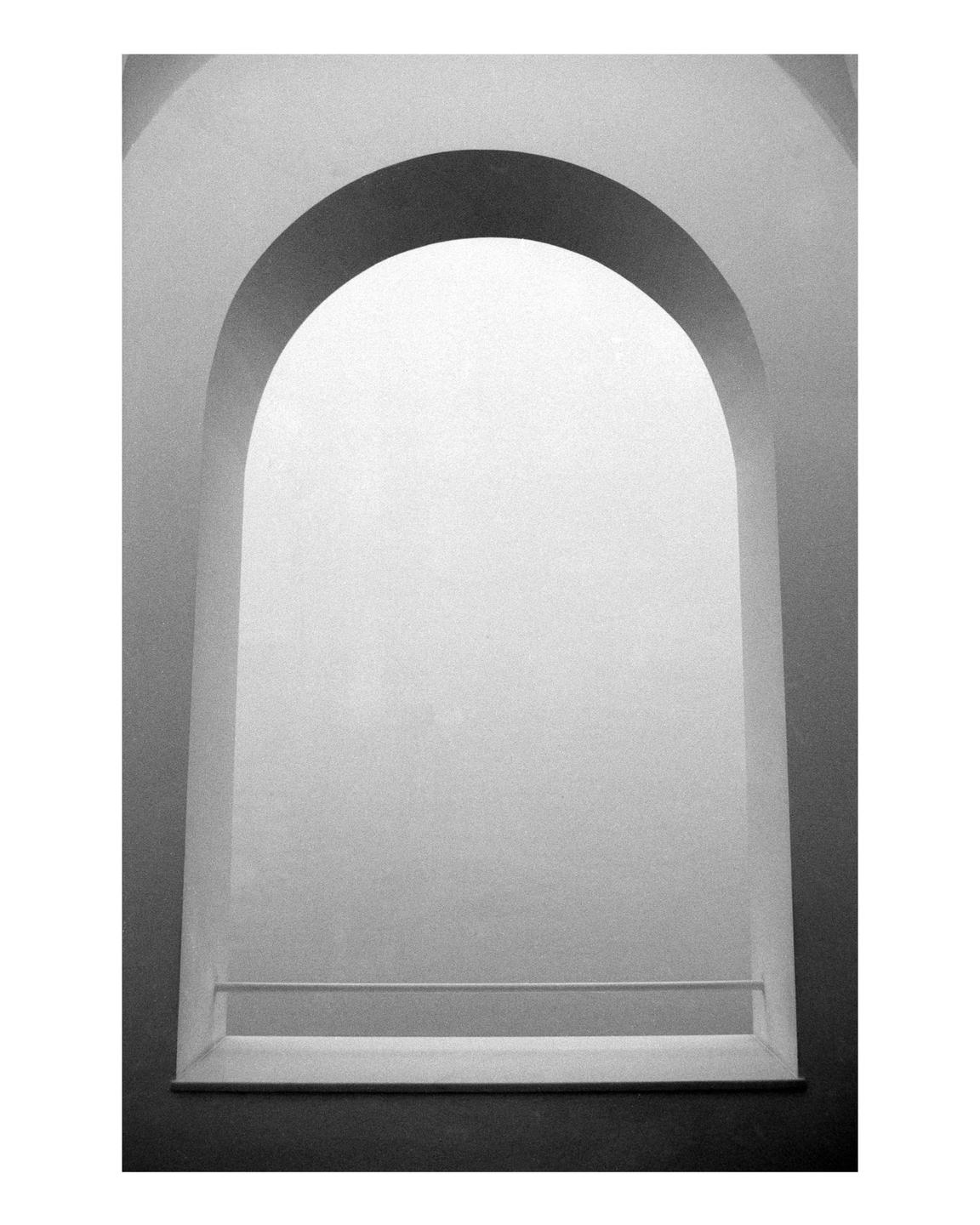 A black and white photograph shows an arched window with a small ledge.