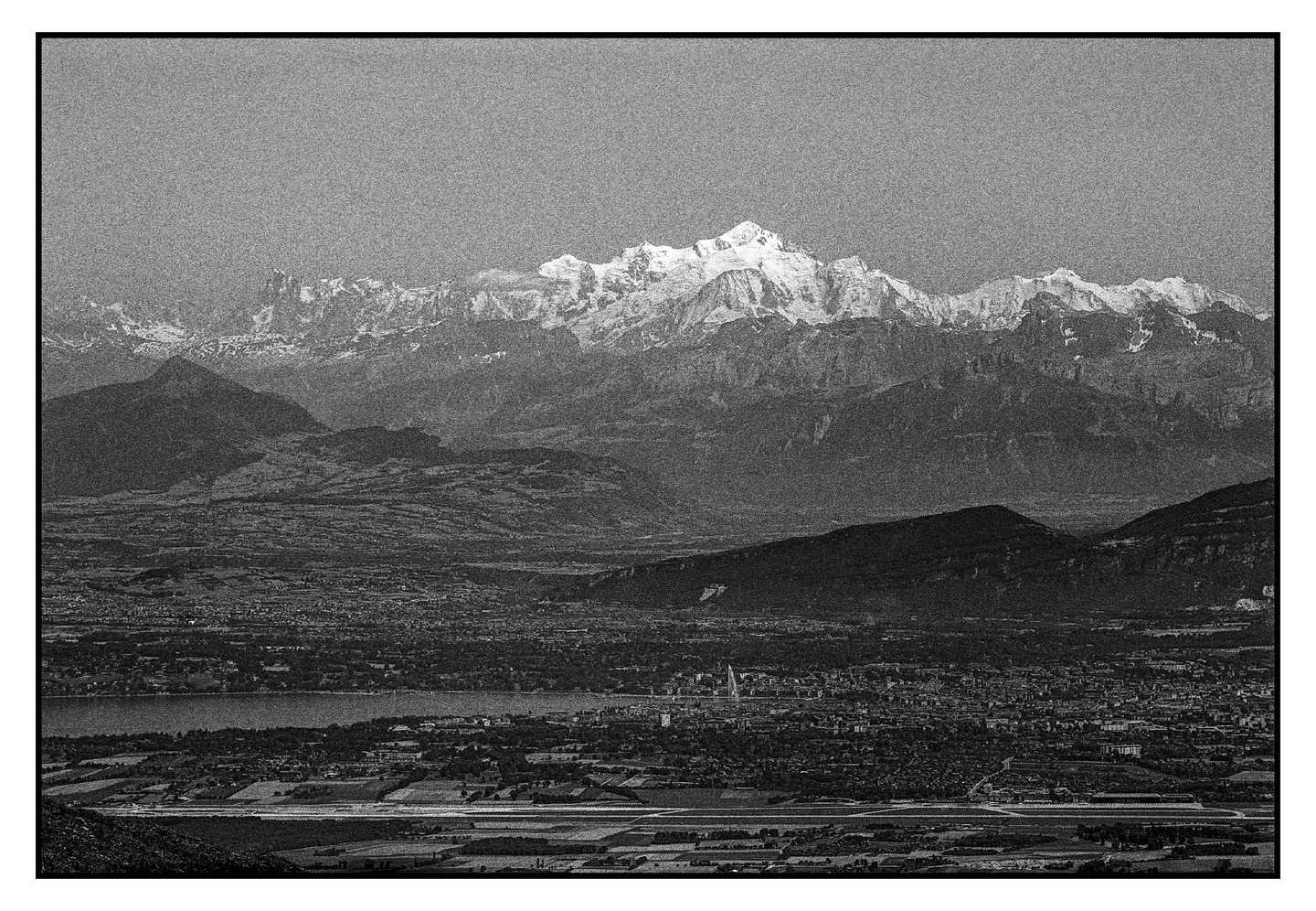 A panoramic view shows a city and lake in the foreground with snow-capped mountains in the distance.