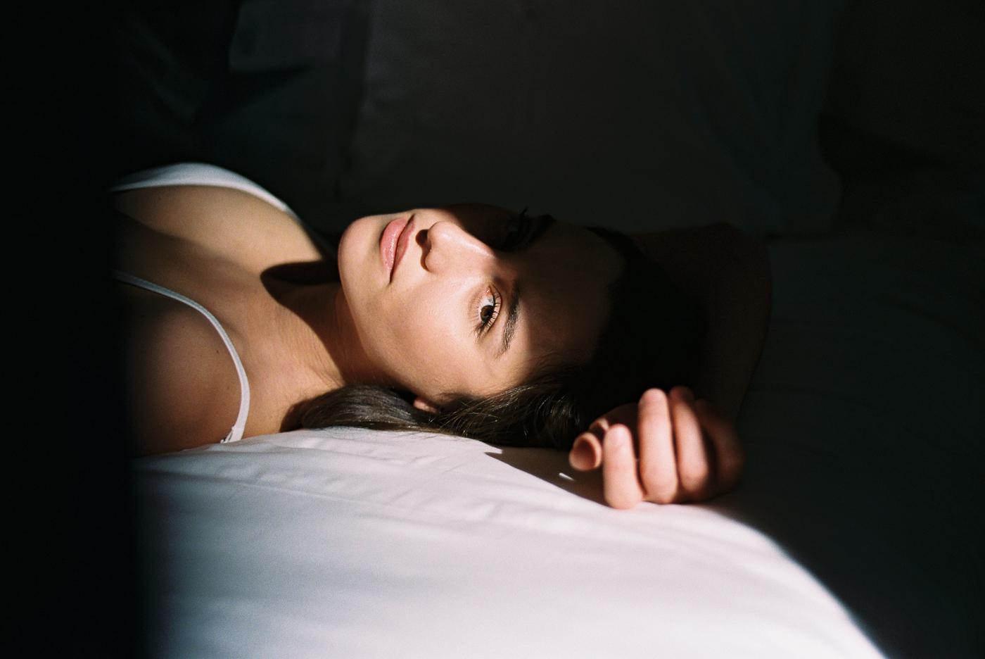 A woman lies on a bed with a beam of light illuminating her face and chest.