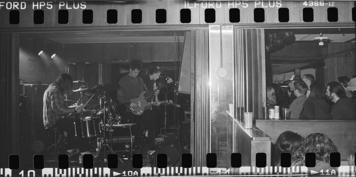 A band performs on stage while people watch from a bar area.