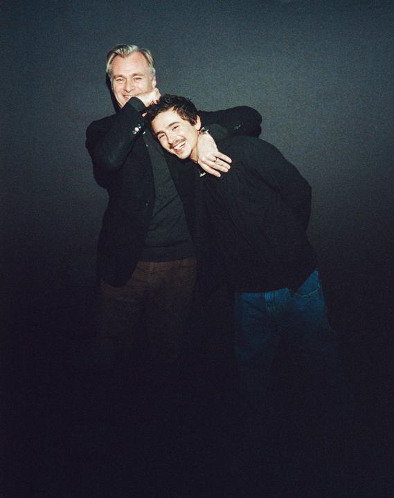 A man with gray hair and a younger man with dark hair are embracing and smiling at the camera.