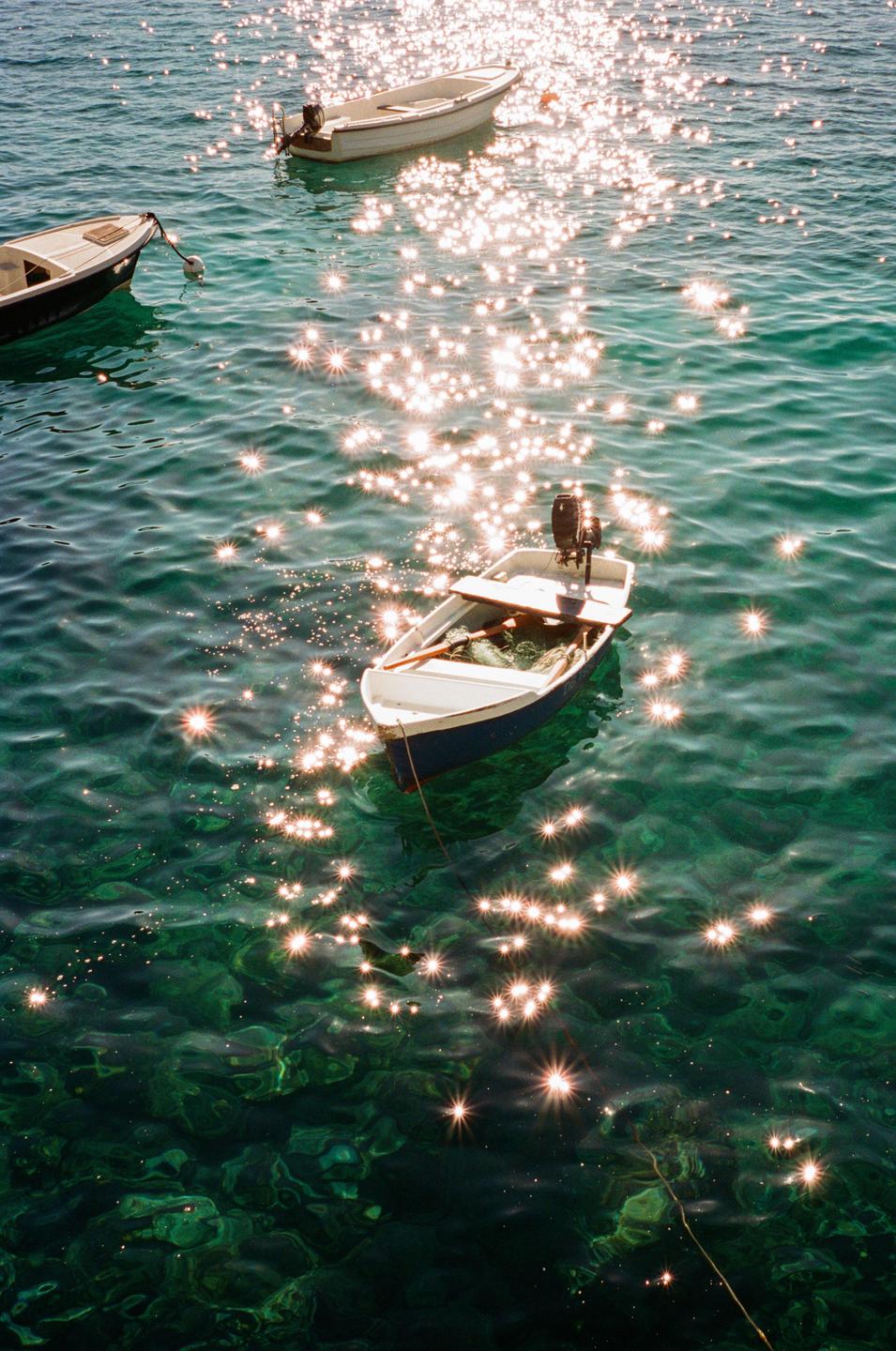 Three small boats float on sparkling green water.