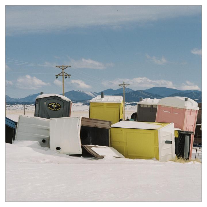 A collection of colorful portable toilets are scattered in a snowy field with mountains in the background.