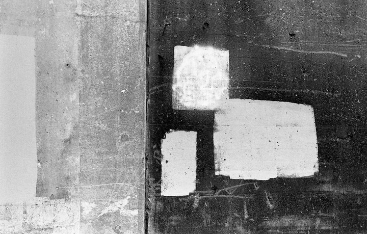 Three white rectangular shapes are painted on a dark, textured surface next to a lighter, textured wall.