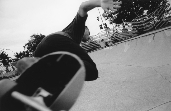 A skateboarder is captured in motion at a skatepark, with a low-angle view of the skateboard in the foreground.