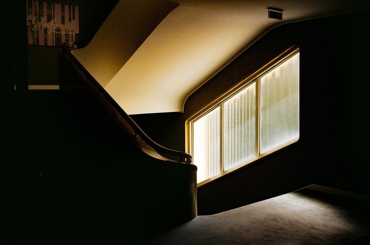 A dark interior features a curved staircase and a large window with frosted glass panels.