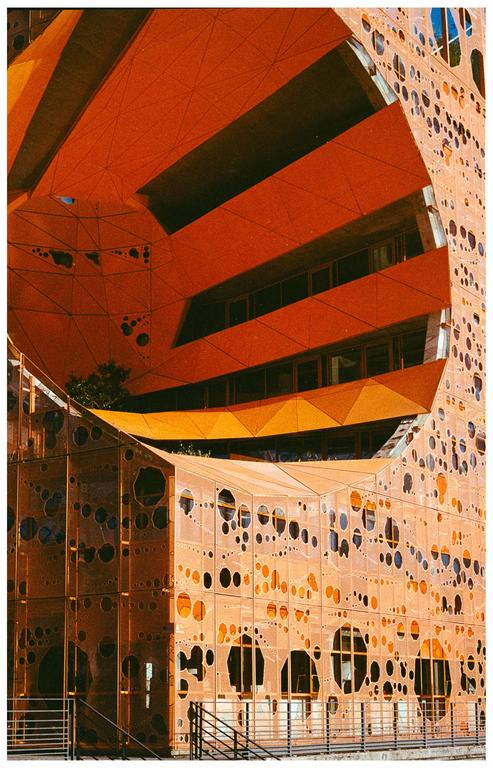 A large orange building with circular cutouts and geometric shapes is shown from a low angle.