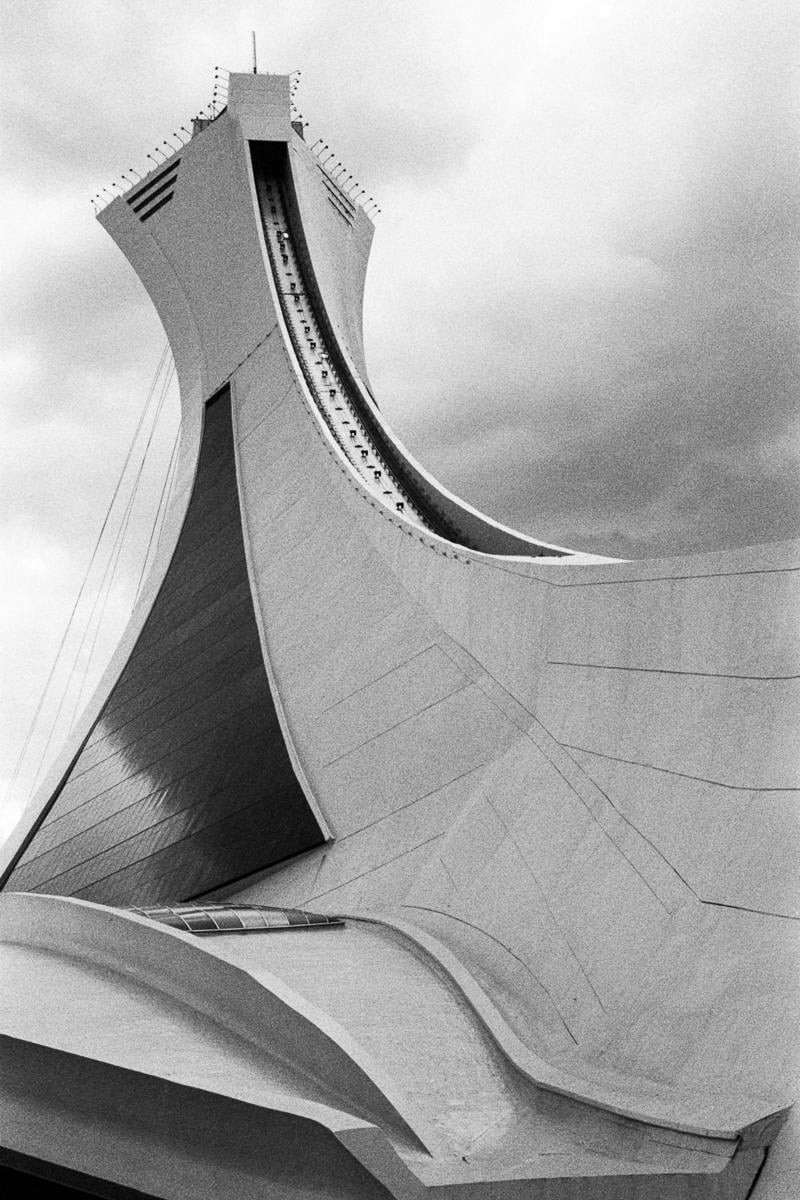 A close-up, low-angle view of the Montreal Olympic Stadium tower shows its curved concrete structure and the funicular track.