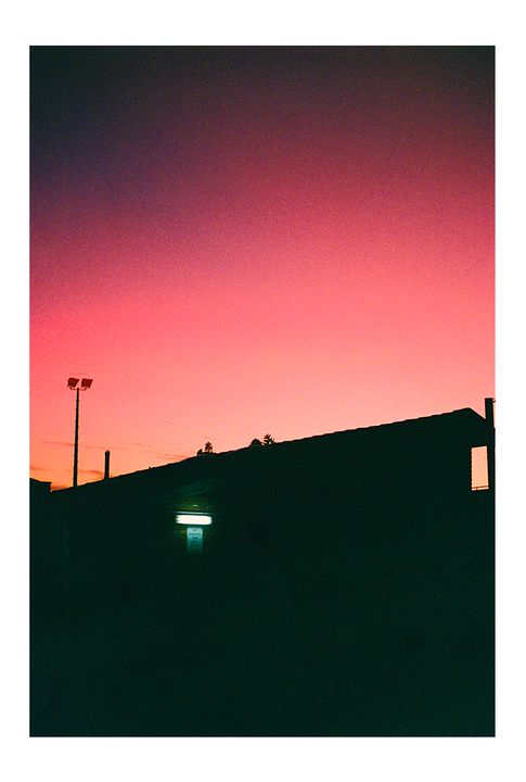 A dark building and a light pole are silhouetted against a vibrant pink and orange sky.