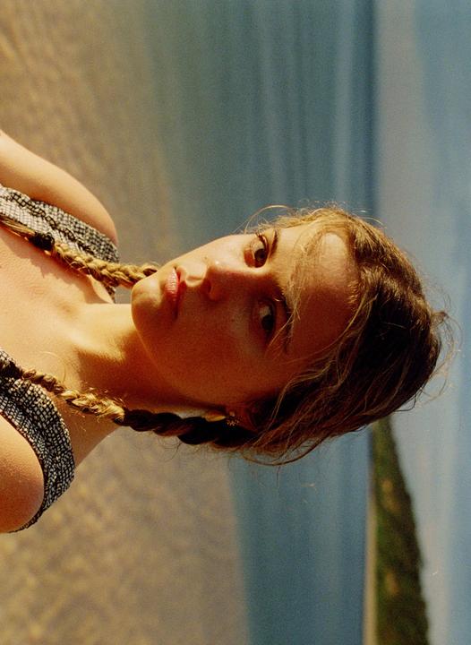 A young woman with braided hair looks directly at the viewer.
