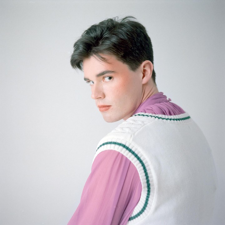 A man with makeup looks over his shoulder at the viewer.