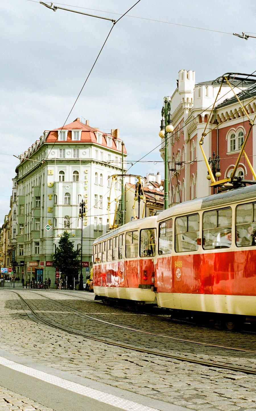 A red and white tram travels along a cobblestone street past historic buildings in Prague.