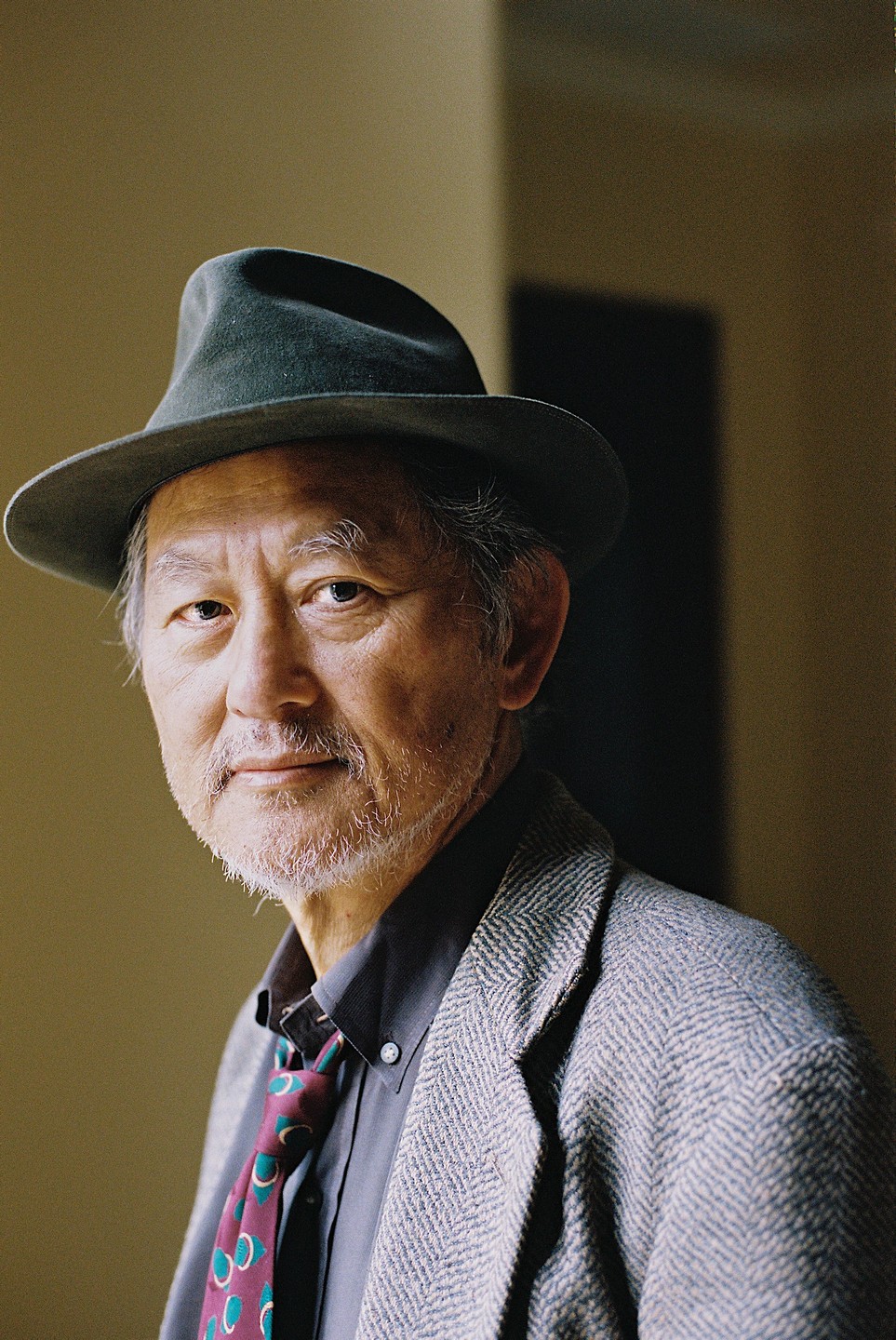 A man wearing a hat, jacket, and tie looks directly at the viewer.